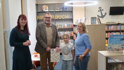 Oberbürgermeister Thomas Feser und Büchereileiterin Julia Löffler (li.) bei der  Gewinnübergabe an Anna Altherr. Auch Mutter Lena freut sich.