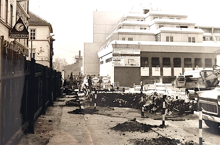 Das Foto zeigt das Karstadt-Haus mit einem Bauzaun zur Basilikastraße.