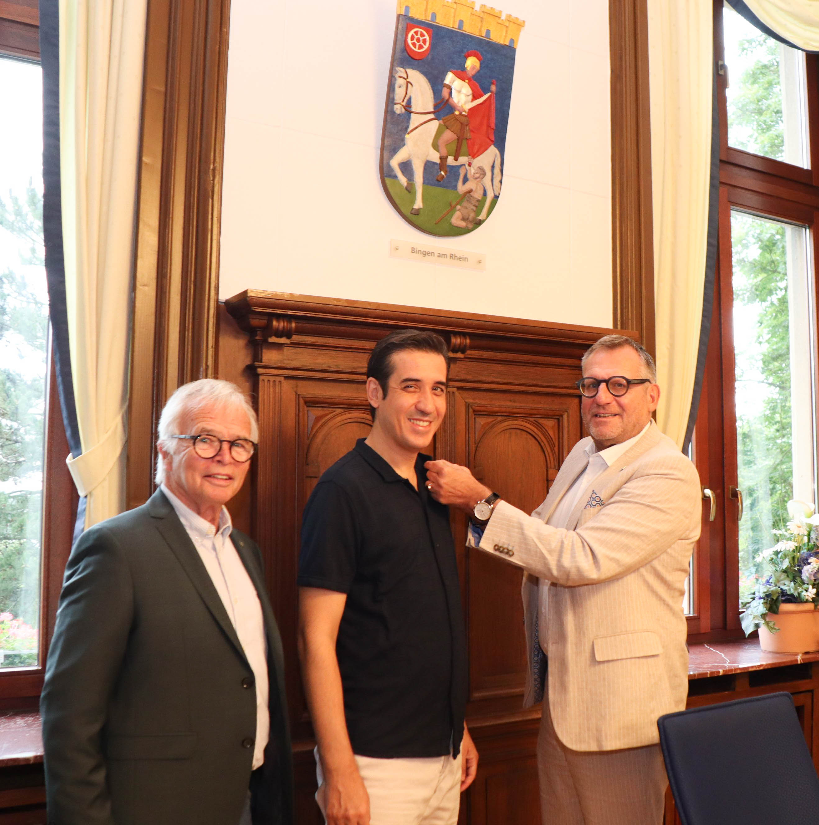 Oberbürgermeister Thomas Feser (re.) überreicht Dr. Tuncay Topsakaloğlu den Ansteck-Pin der Stadt Bingen. Links im Bild: Helmut Irmen, der Vorsitzende des Freundschaftskreises Bingen-Anamur.