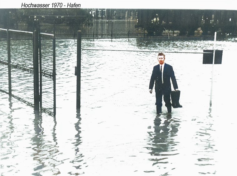 Ein Mann im Anzug steht in der Hafenstraße im Hochwasser und trägt Gummistiefel in der Hand, 1970.
