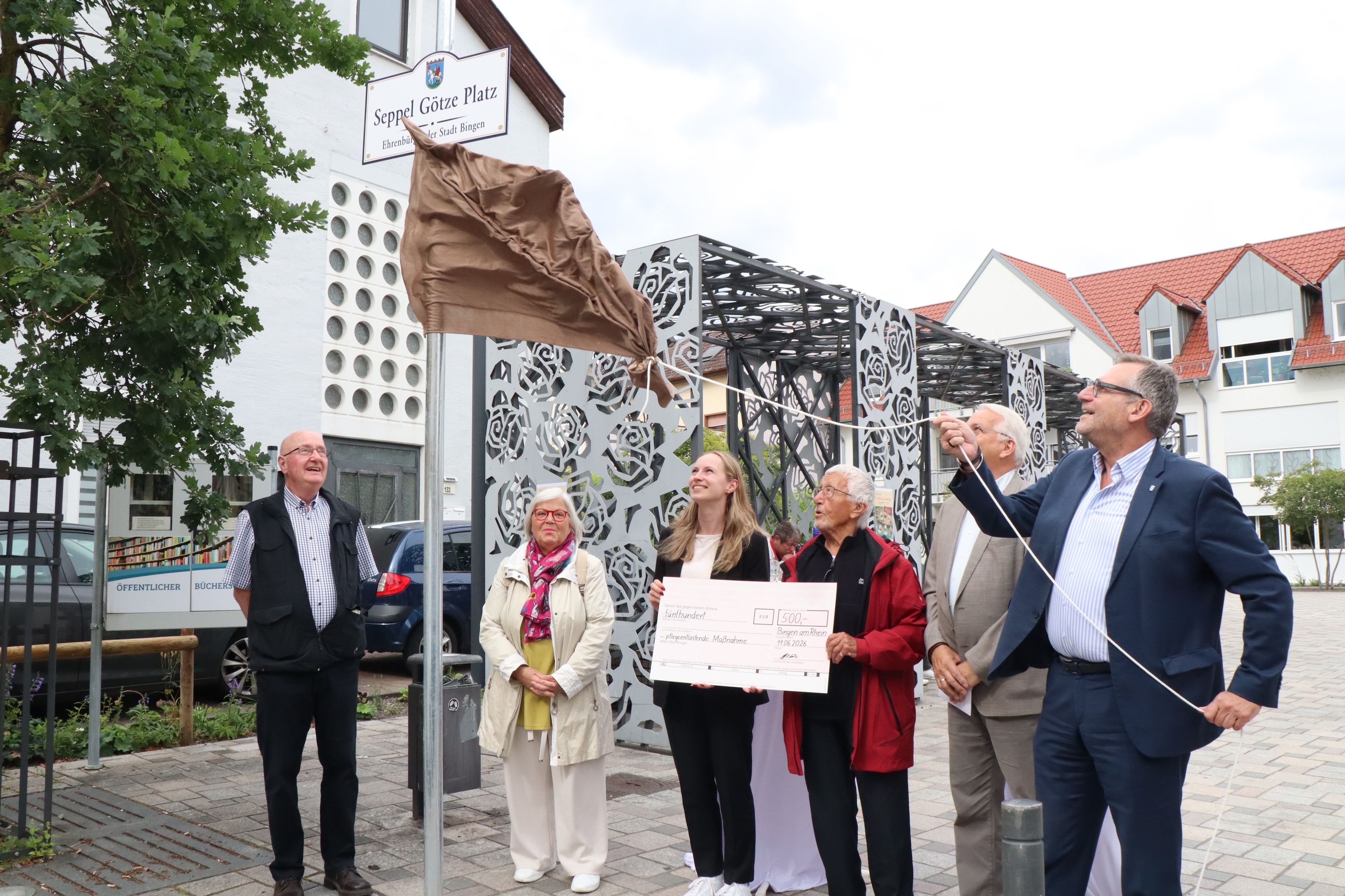 Werner Velten (SPD), Ursula Hartmann-Graham (Vorstand Bürgertreff Büdesheim), Diana Franke, Seppel Götze, Michael Porr und Oberbürgermeister Thomas Feser (v. li.) bei der Enthüllung des Schildes.