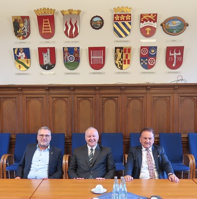 Oberbürgermeister Thomas Feser (li.) dankte Hasan Eker und Hüseyin Baraner (re.) im Sitzungsaal von Burg Klopp (im Hintergrund die Wappen der Binger Stadtteile und der Binger Partnerstädte) für das Gespräch und die eingebrachten Anregungen.